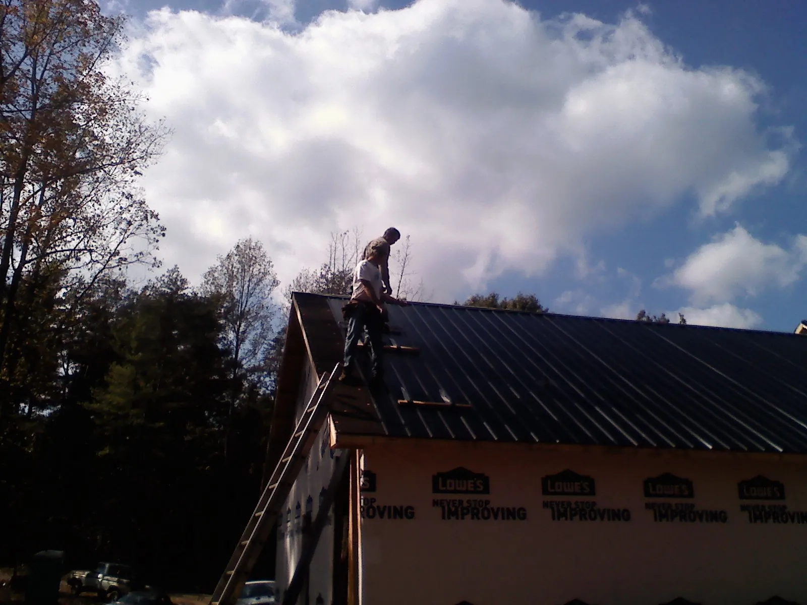 Roofer fastening dark metal panels high against a cloudy sky, from a Roof Inspection job in New Preston Marble Dale