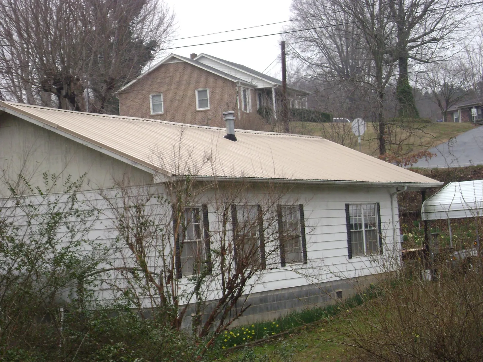 Tan metal roof on a white sided house set into a hillside — Commercial Roofing by Roofing Brothers in New Preston Marble Dale